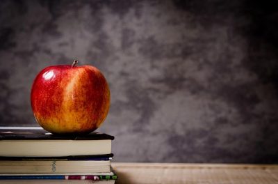 education illustration: apple on top of books with blackboard in background.