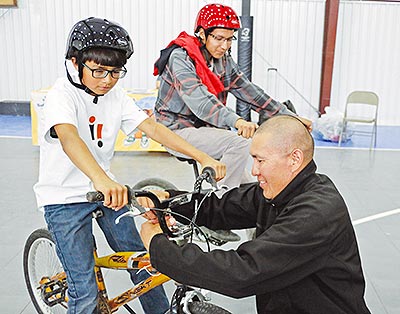 Marquis Yazzie, left, gets his bike worked on by Toby Tsosie while Darlando Nez watches during the Bike Rodeo event on March 25 in Dilkon, Ariz. (Times photo-Stacy Thacker)