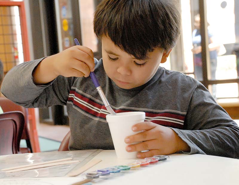 Isaiah Fuller, 9, from Oak Springs, Ariz. works with a paintbrush to color the t’iis bitł’óól sticks for the Navajo stick game. (Times photo – Shondiin Silversmith)