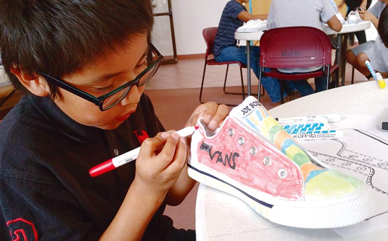 Ten-year-old Xavier Nelson from St. Michaels, Ariz. works on his shoes during the Rezzy Feet event last week. Nelson said he came to the museum to read at the library and was happy to participate in the event. (Times photo – Shondiin Silversmith)