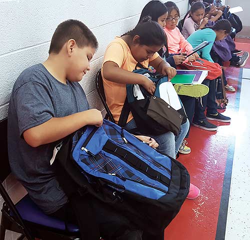 Students look through their new backpacks in the gym at Kin Da Lichi’i Olta’ on Friday. The Morning Star Leaders Youth Council out of Phoenix held the drive after an employee of the school wrote them about the need of the students in Kinlichee, Ariz. (Times photo – Stacy Thacker)