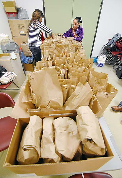 Navajo Times | Donovan Quintero Miss Tsaile Junior High Natiana King, right, and her mother Roxyanne Harvey, finish placing pieces of frybread into paper sacks Nov. 25 at the Sycamore Community Center in Farmington. 