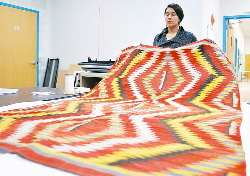 Navajo Times | Ravonelle Yazzie Museum volunteer Rebecca Heidenreich lays out a hand carded and spun Eyedazzler Blanket for the new Jó Jiní exhibit at the Navajo Nation Museum. Navajo Nation Museum.
