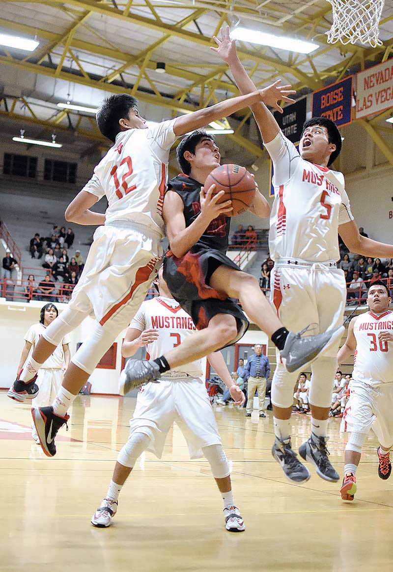Navajo Times | Donovan Quintero Santa Fe Indian School Brave Francis Calabaza, middle, soars between Monument Valley Mustangs Royce Charley (12) and Irwin Holiday (5) Saturday night during the championship game at the 5th annual Striking Eagle Native American Invitational in Albuquerque. 