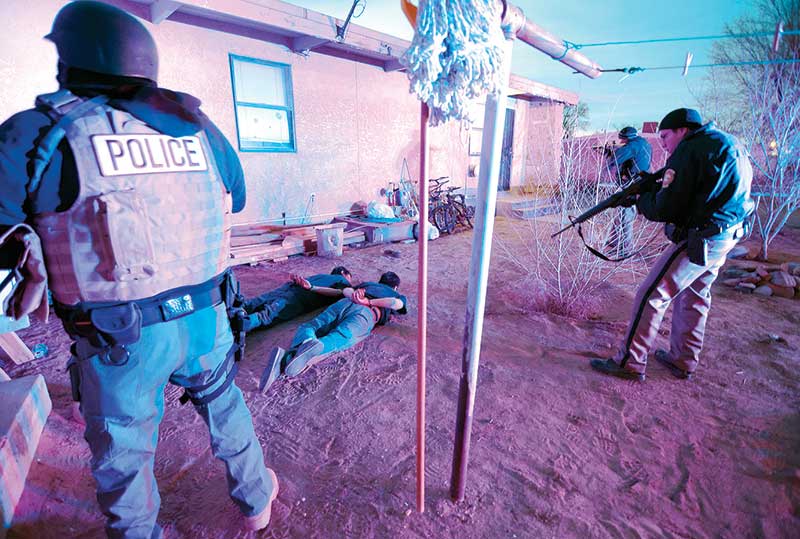 Navajo Times | Donovan Quintero In this Feb. 12, 2014 file photo, Navajo police officers closely keep watch on two men who lie handcuffed on the ground early Wednesday morning after executing a search warrant in Shiprock.