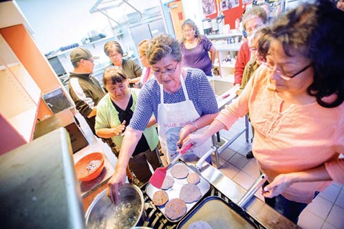 Navajo Times | Adron Gardner Sandra Deswood, left, assists Lillie Pete with dah'njilo'ii as Ruth James turns blue corn pancakes during the Navajo Wellness Model Conference.