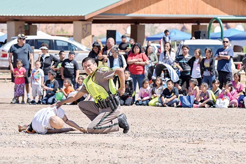 Navajo Times | Krista Allen Onlookers watch as Police Sgt. Byron Coolie of the Kayenta Police District reaches for his radio and waits for first responders to arrive to the scene of a mock car crash in which a person was ejected from a truck containing five individuals on May 13, during Public Safety & Law Day in Kayenta.