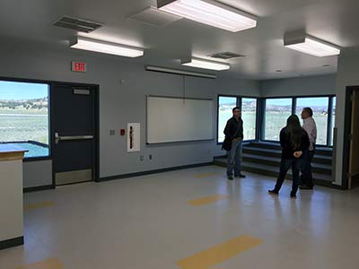 Three people stand in empty classroom with windows overlooking outdoors