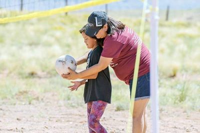 Woman leans over girl, holding volleyball.