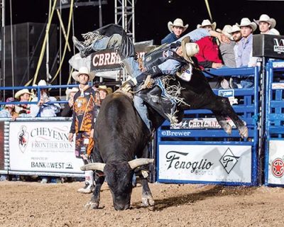 Bull rider hangs onto bucking bull with one hand, other swung over his head.