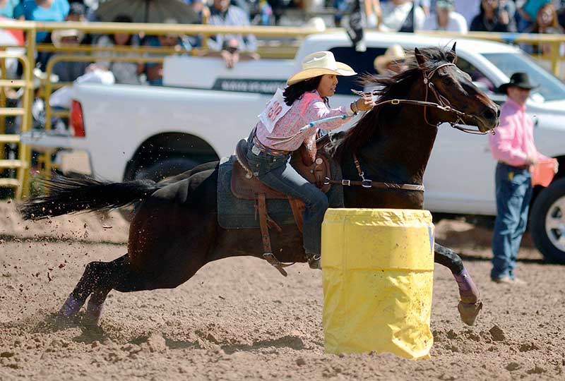 Girl on horse races past yellow barrel.