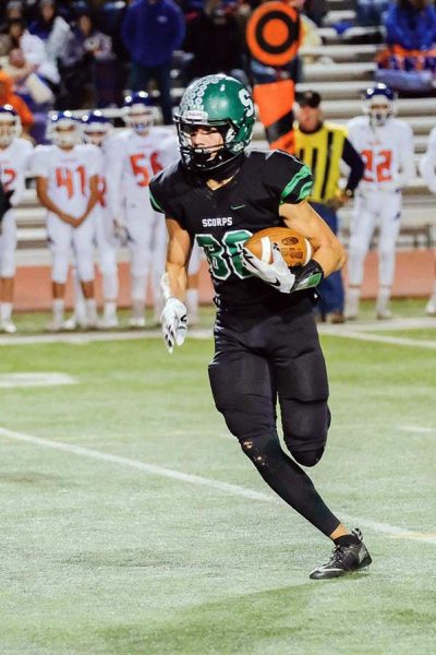 Runner cradles ball on football field alone.