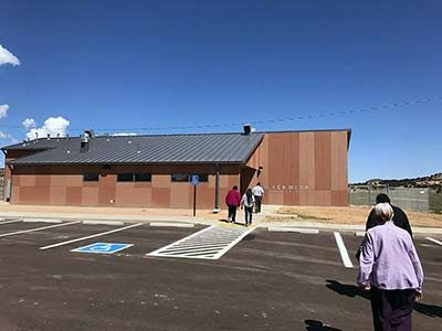 People walk across empty parking lot to new building.