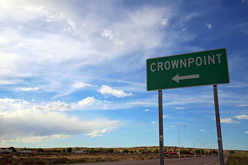 Road sign indicating direction to Crownpoint, against large cloudy sky.