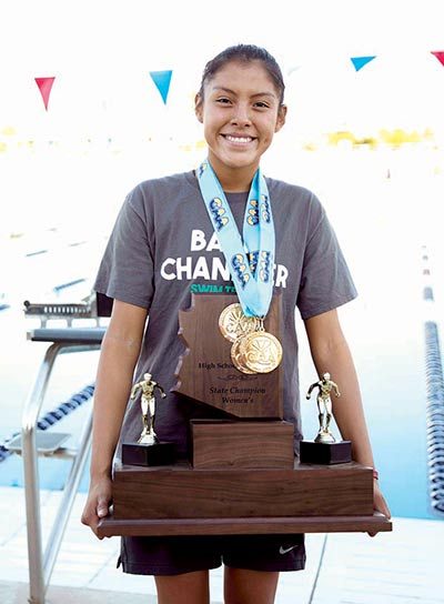 Girl holds giant trophy, with gold medals around neck.